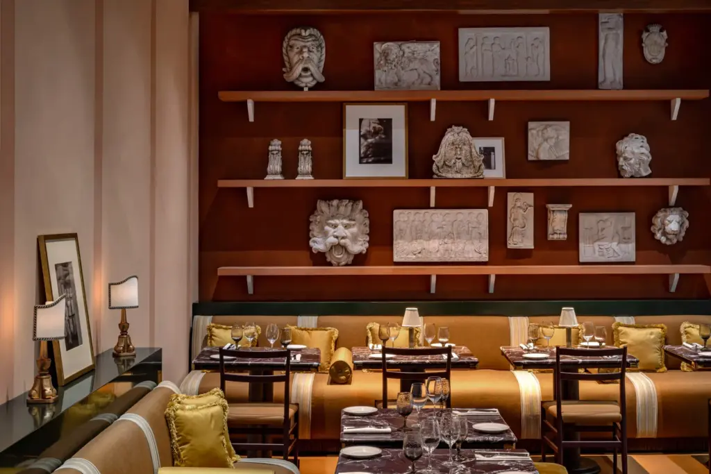 Salle du restaurant d’Experimental Roma, avec banquettes, tables dressées et mur décoré de reliefs et de cadres