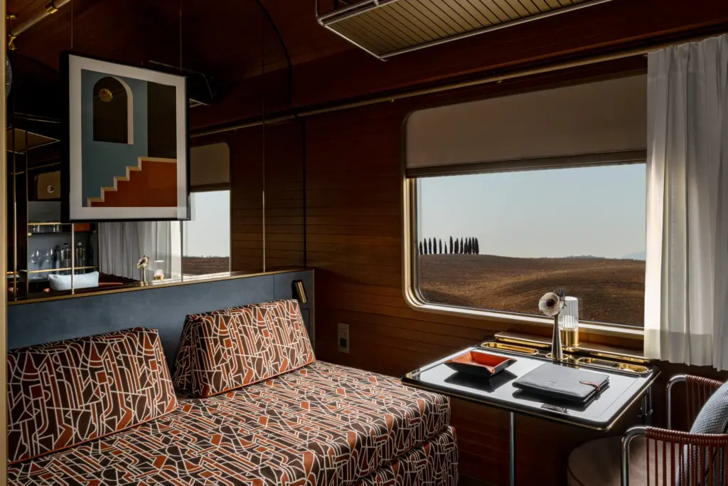 Cabine de La Dolce Vita Orient Express, banquette à motifs géométriques, boiseries et fenêtre ouverte sur la campagne toscane