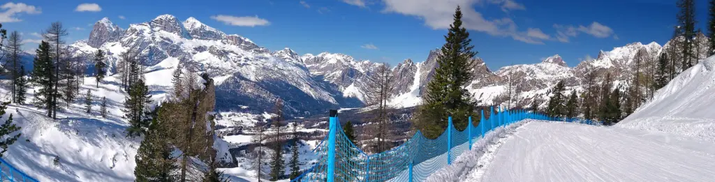 Panorama hivernal de Cortina d’Ampezzo et des Dolomites depuis une piste bordée de filets