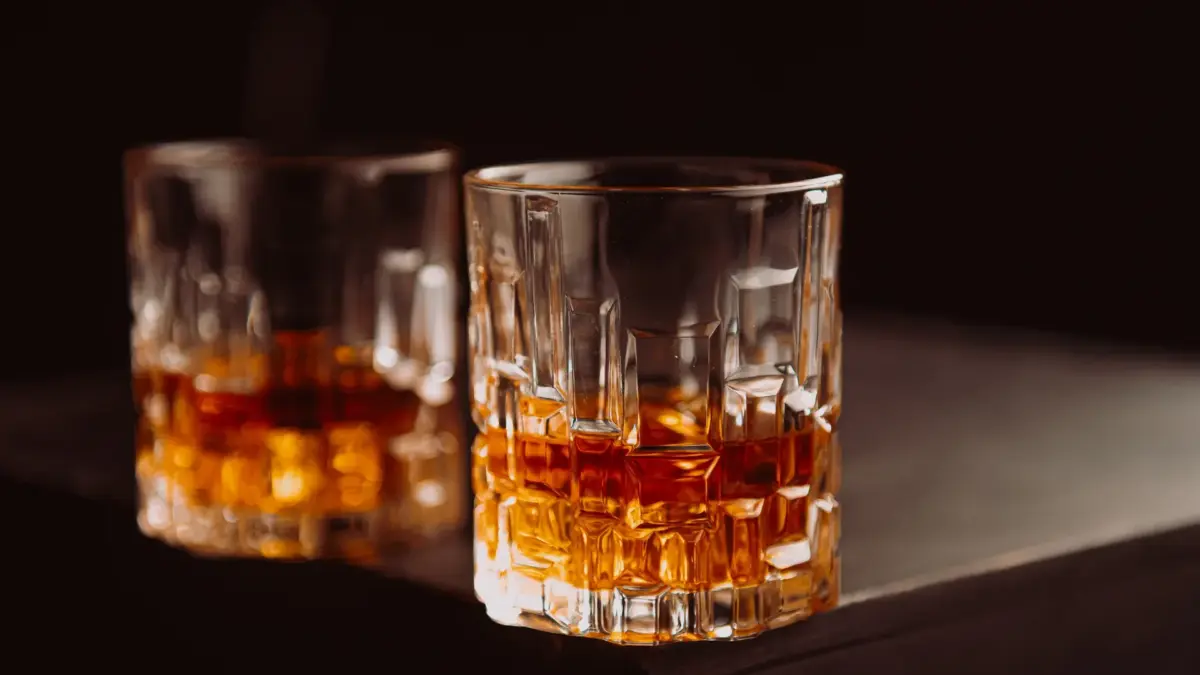 Deux verres à whisky ambré posés sur une table sombre, l’un net au premier plan