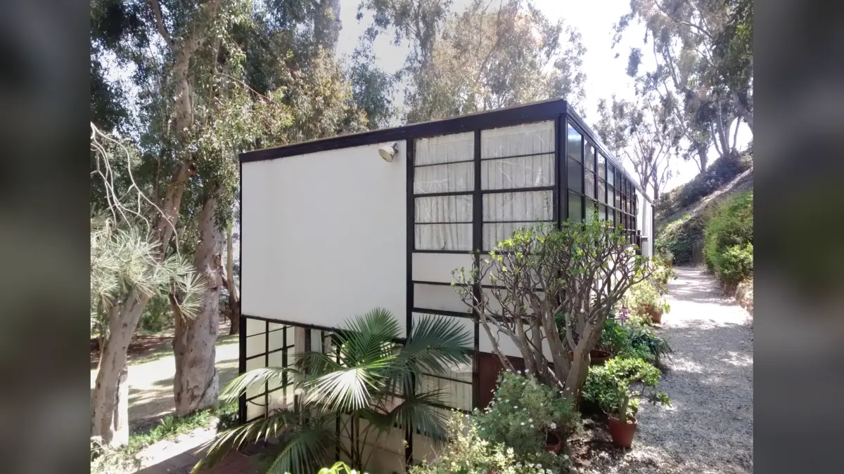 Façade vitrée de l’Eames House bordée d’arbres et de plantes dans un jardin boisé