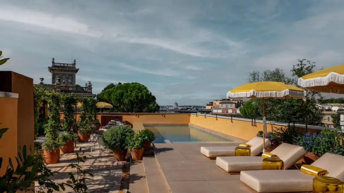 Piscine sur le toit de l’hôtel Experimental Roma, transats et parasols jaunes face aux toits de Rome et à la coupole de Saint-Pierre