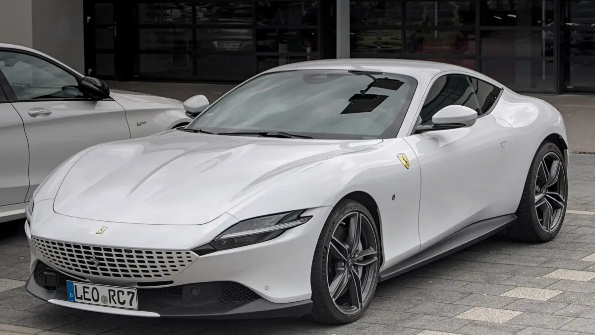Ferrari blanche garée devant une vitrine, vue de trois quarts avant sur un parvis pavé