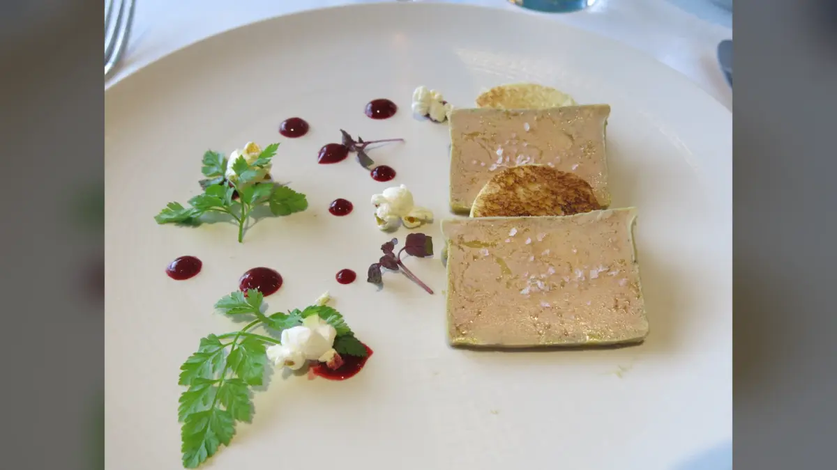 Deux tranches de foie gras dressées avec gelée rouge, herbes et fleurs sur assiette blanche