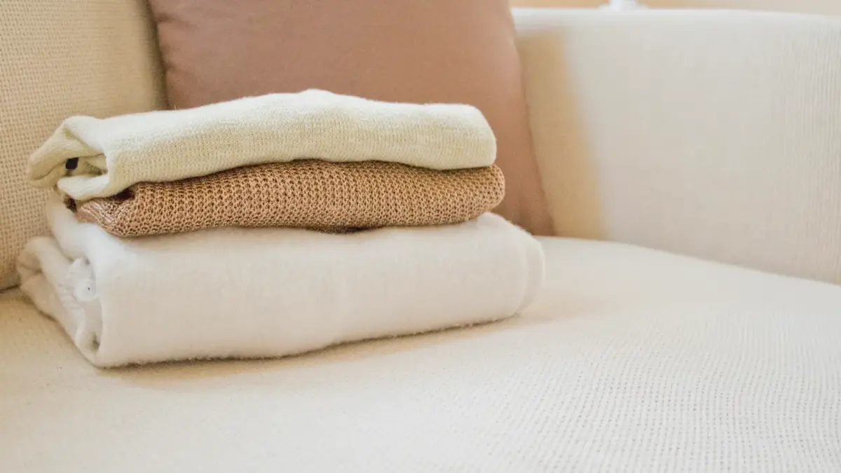 Pile de pulls en cachemire pliés dans des tons crème et beige sur un canapé clair
