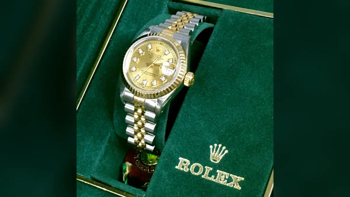 Montre Rolex bicolore à cadran doré serti, posée dans un écrin vert à logo brodé