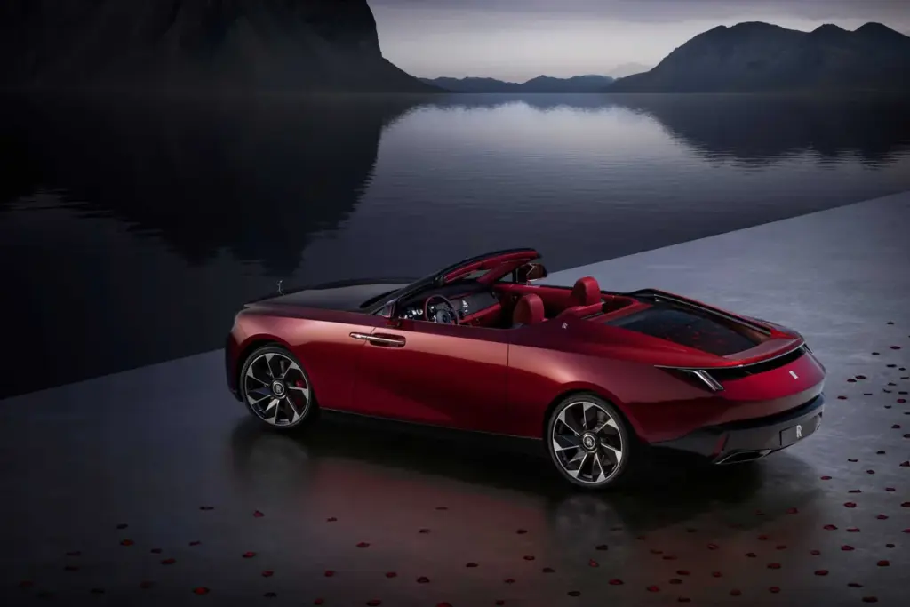 Rolls-Royce La Rose Noire Droptail rouge, toit retiré, au bord d’un lac au crépuscule, pétales sur le sol