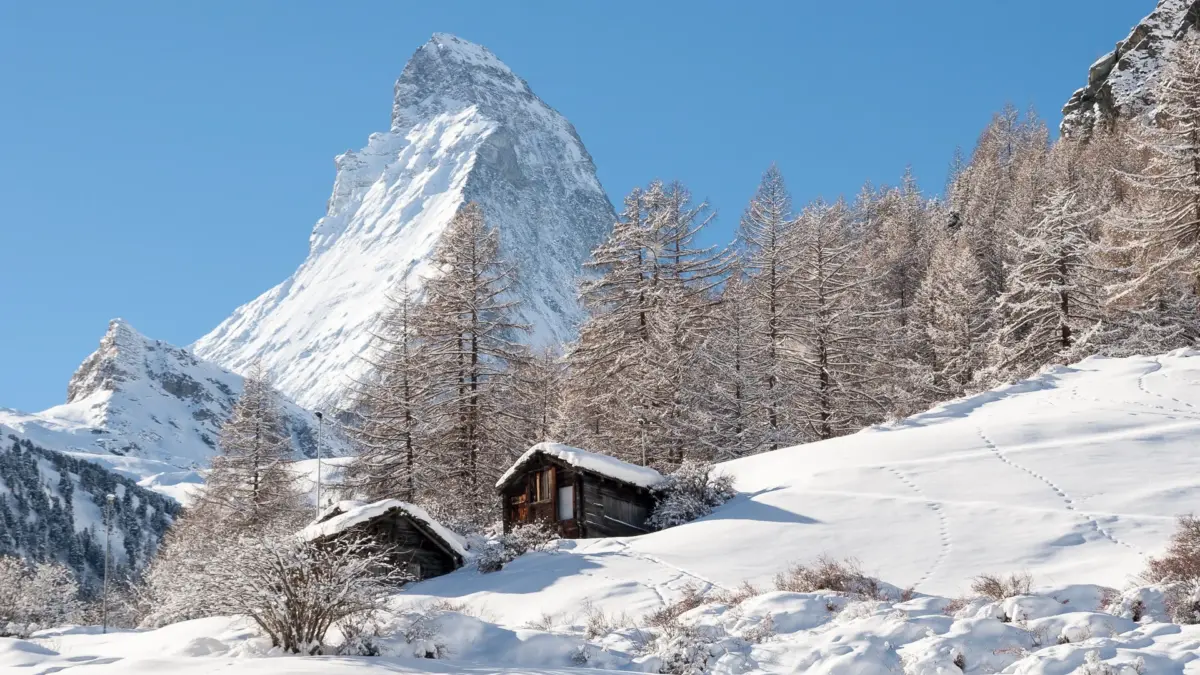 Le Cervin enneigé sous un ciel bleu au-dessus de Zermatt, mélèzes givrés et vieux raccards en bois dans la neige