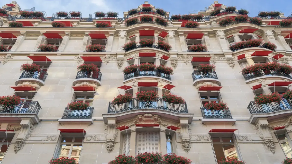 Façade du Plaza Athénée avec balcons fleuris et stores rouges sur l’avenue Montaigne