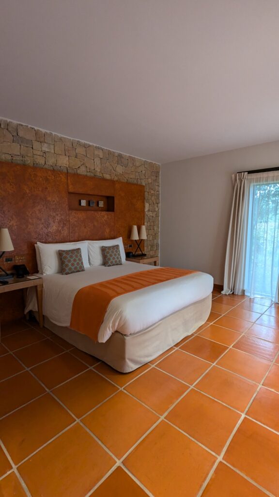 Chambre de notre suite, avec grand lit blanc, tête de lit ocre et sol aux teintes de terre cuite