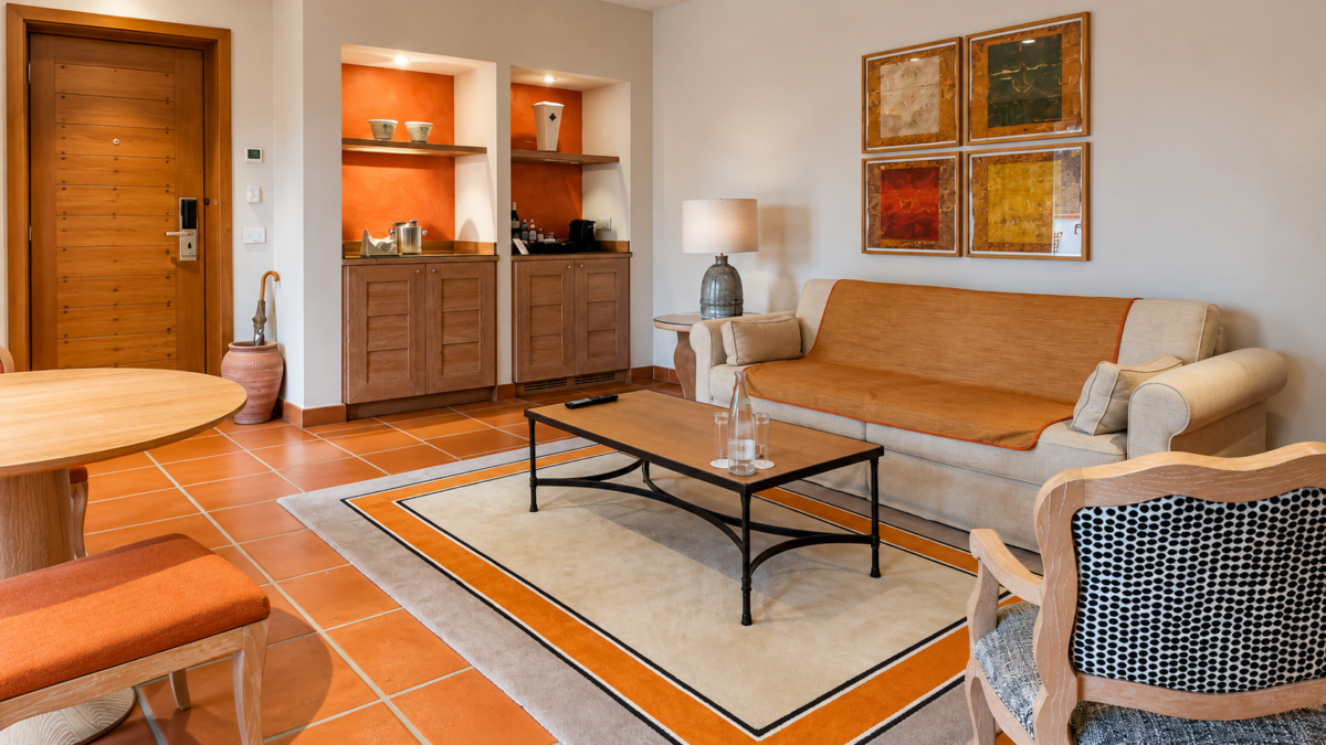 Salon d’une suite de Terre Blanche : canapé clair, sol en terre cuite, tapis à bordure orangée, niches éclairées et quatre tableaux